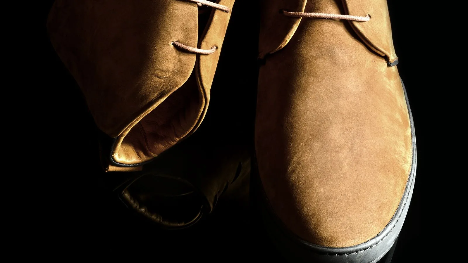 Elegant brown suede shoes with laces on a reflective black surface, showcasing modern fashion.