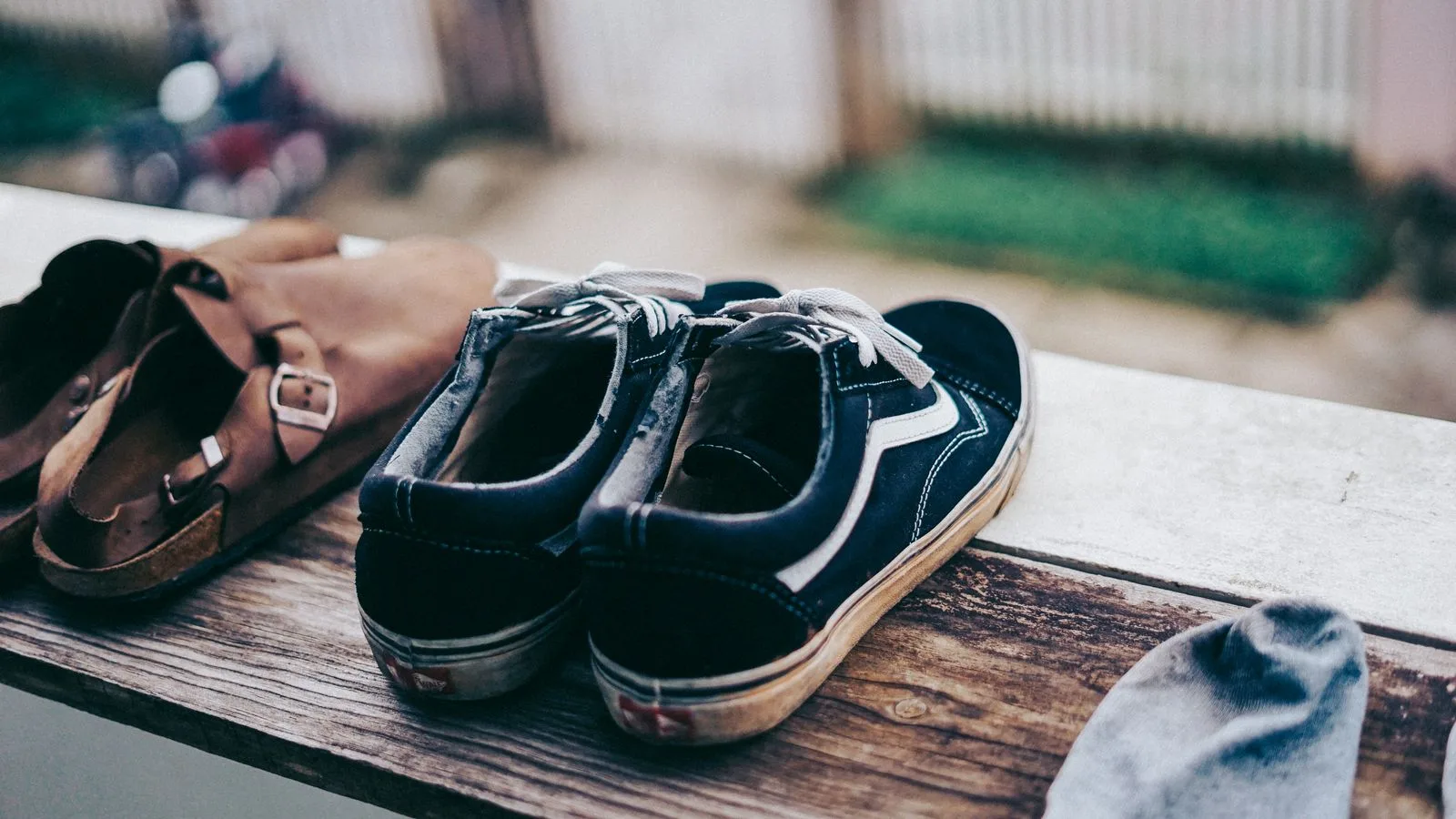 Close-up of casual sneakers and sandals drying on a wooden balcony ledge.