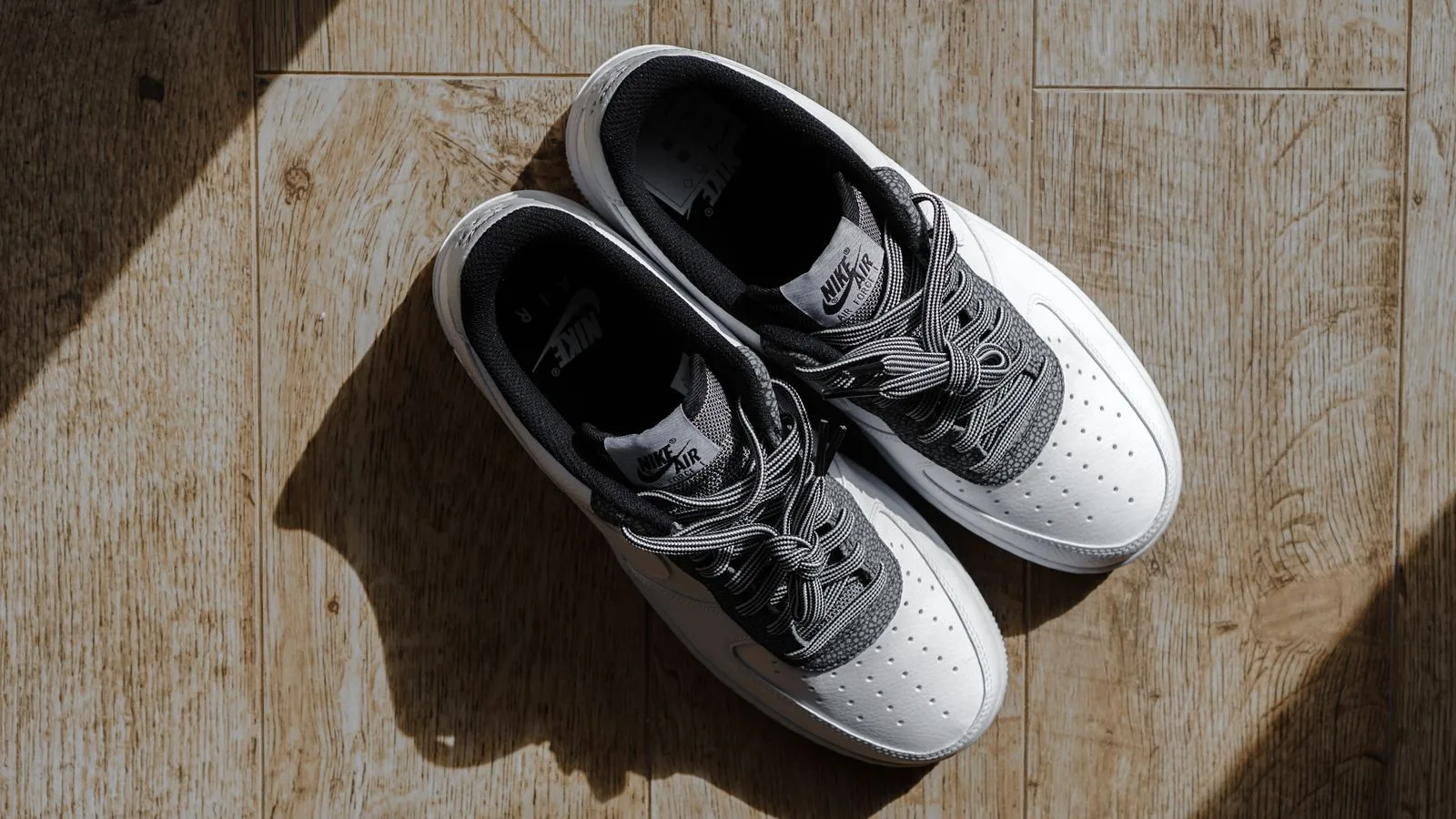 White sneakers displayed on a wooden floor with natural lighting, showcasing fashion footwear.
