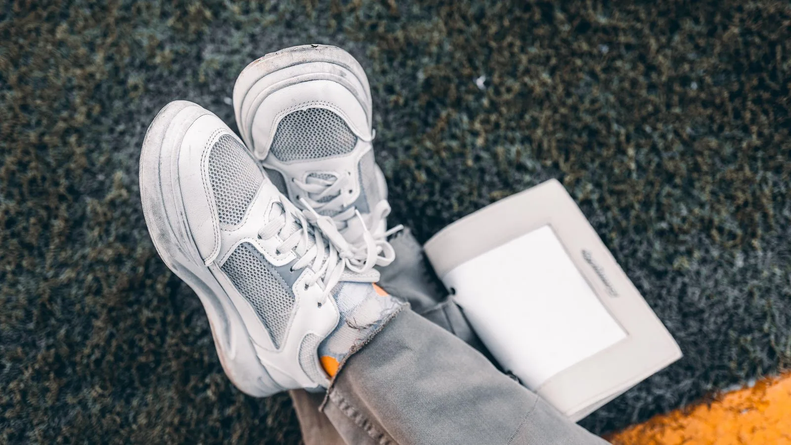 White sneakers casually placed on grass with an open book, conveying a relaxed outdoor vibe.