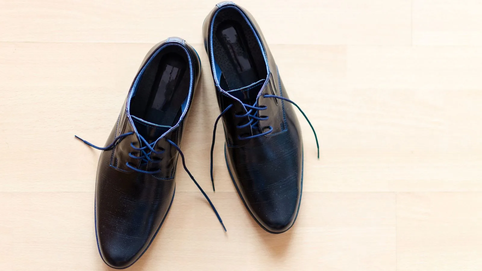 Pair of stylish black leather shoes with blue laces on a wooden floor.