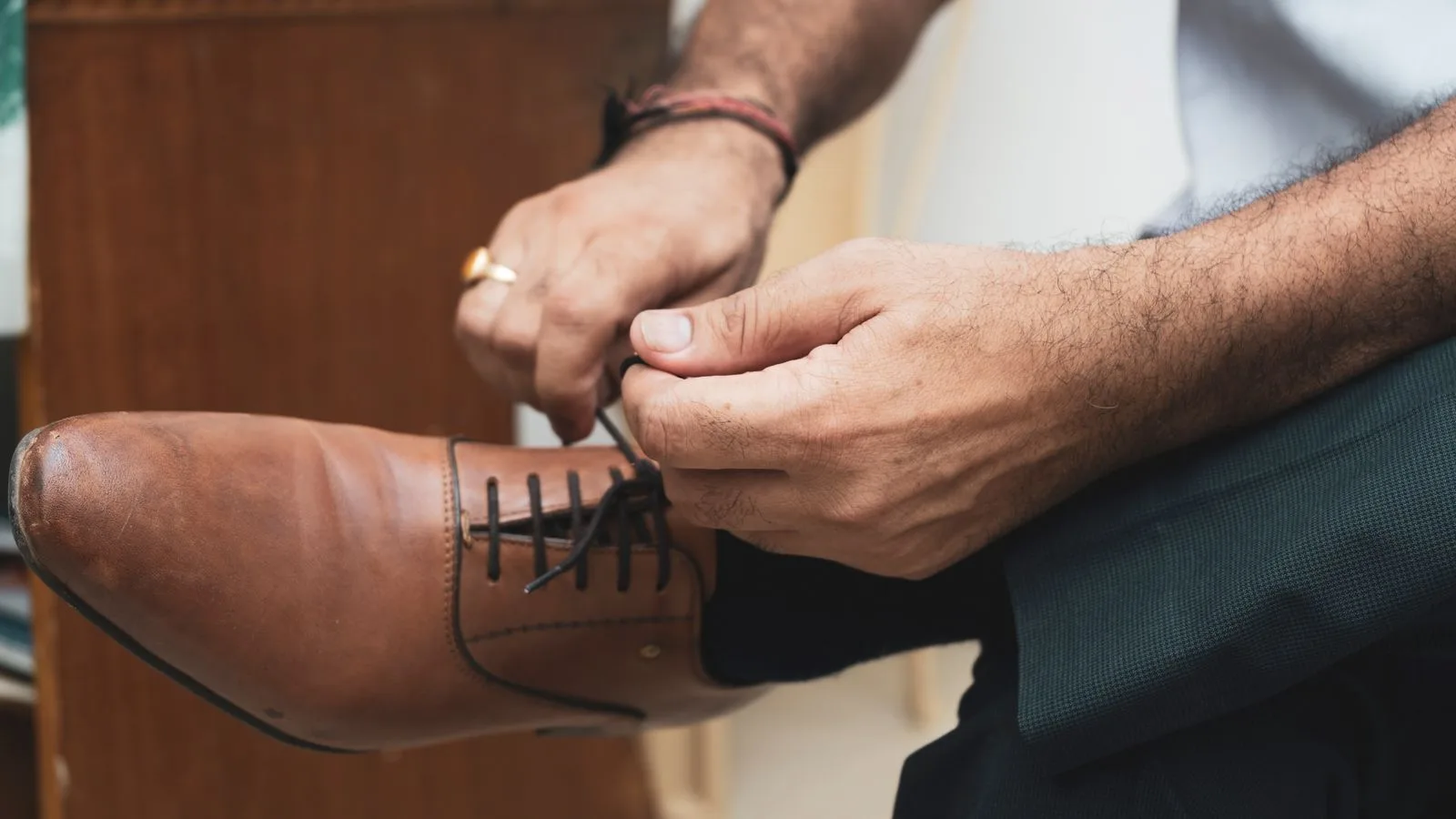 Detailed view of a man tying shoelaces on stylish brown leather shoes indoors.