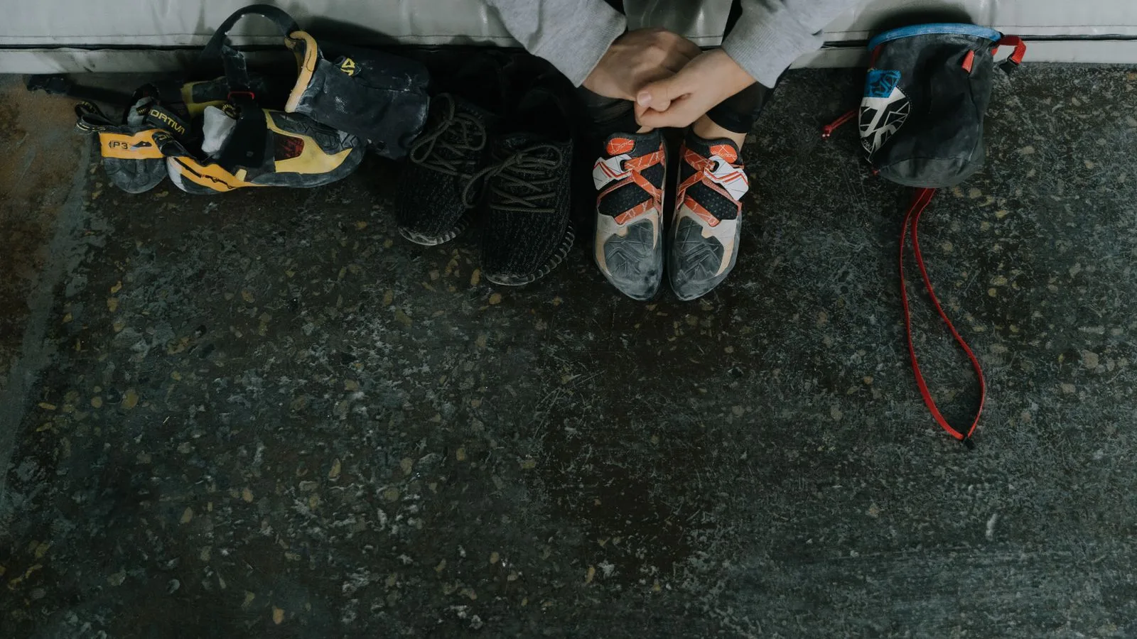 An overhead view of rock climbing shoes, chalk bag, and sneakers on a gym floor.