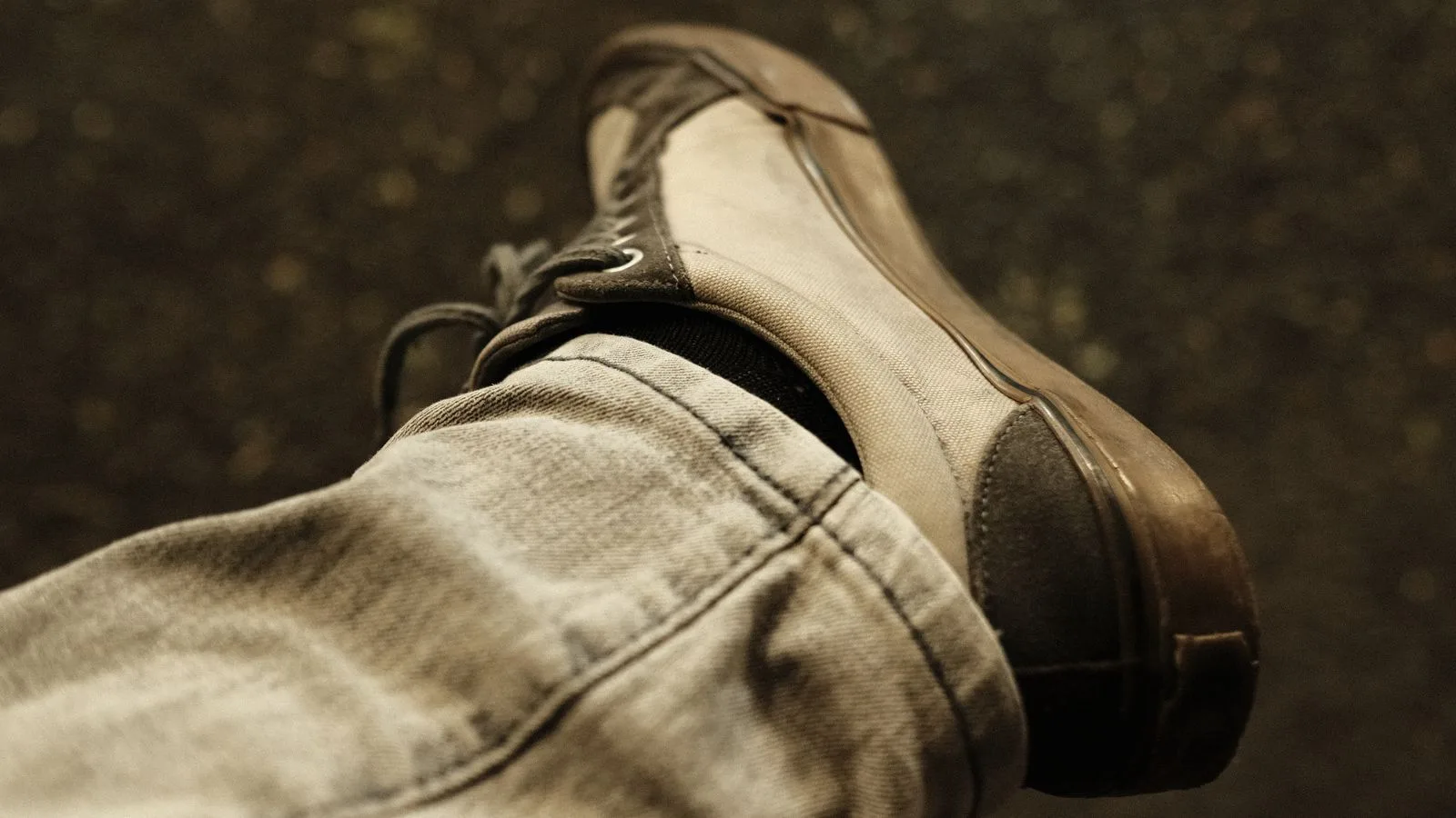 A close-up of a sneaker in sepia tones showcasing casual fashion on a textured street background.