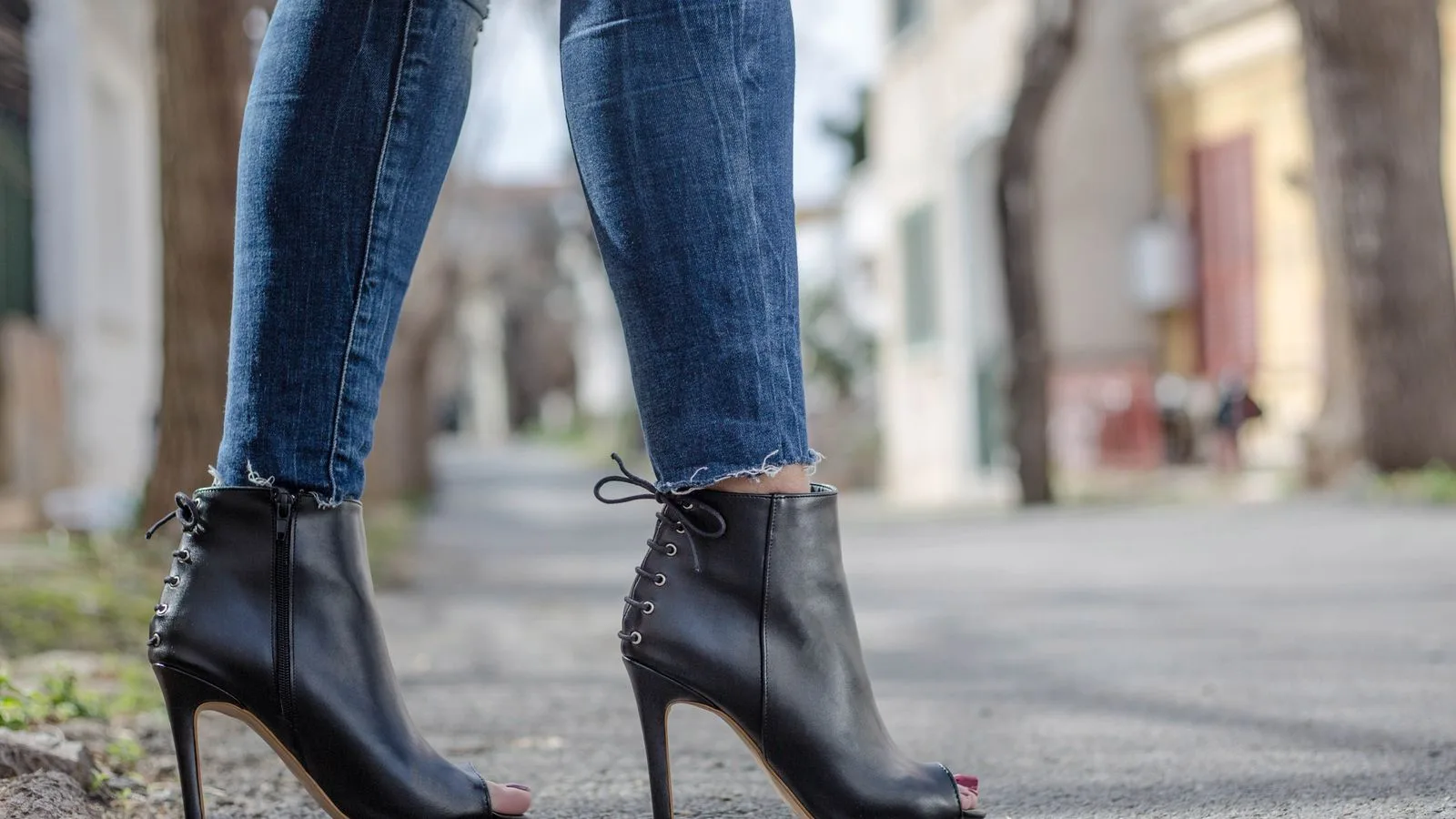Close-up of woman wearing peep toe stilettos with jeans in an urban environment.
