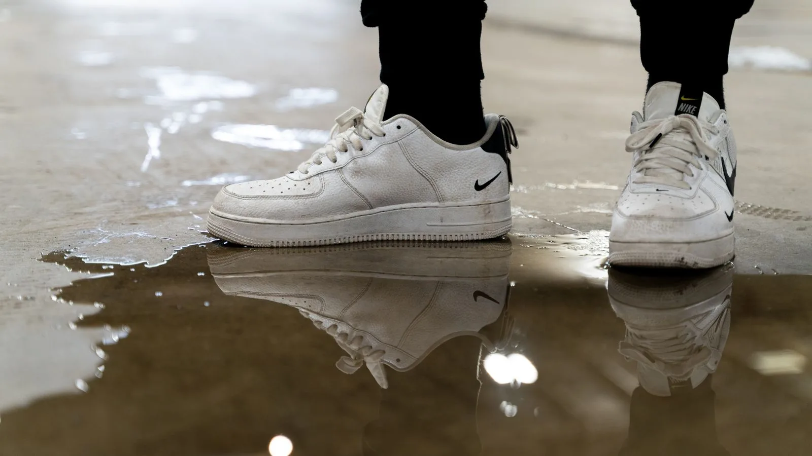 A pair of white sneakers reflected in a puddle on an indoor surface, creating an artistic perspective.