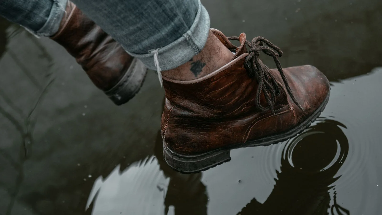 Brown leather boots stepping in a puddle with clear water reflection.