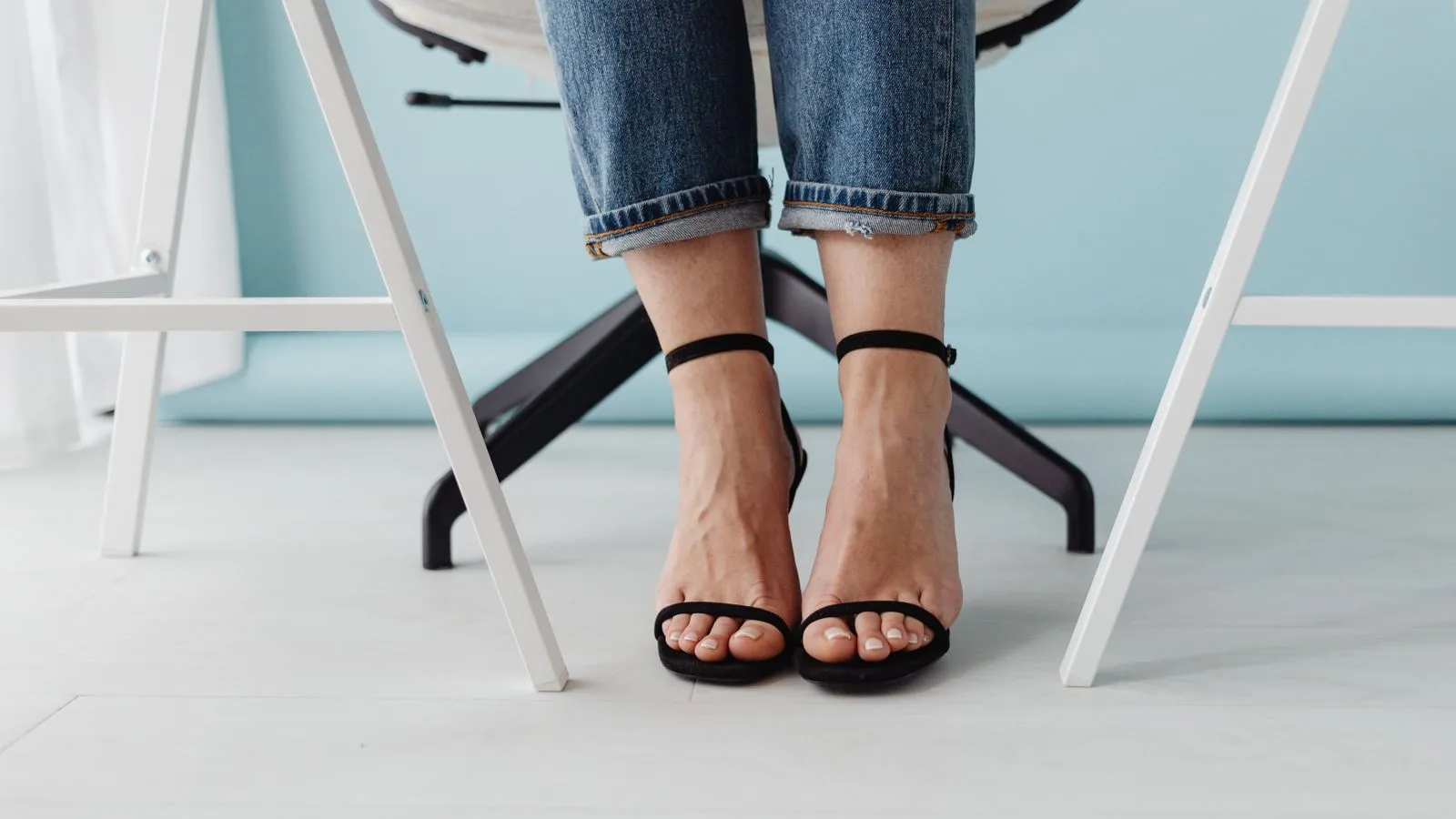 Stylish close-up of a woman wearing black high heels, jeans, and sitting on a chair.